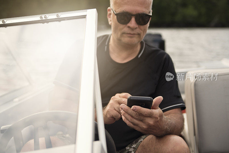 50 + man using mobile phone on small boat on a lake.